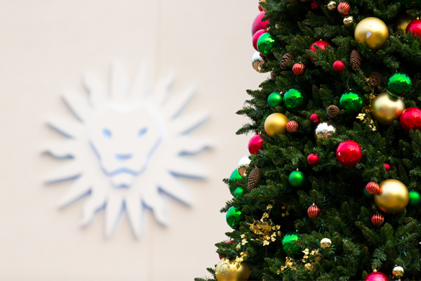 A partial view of a Christmas tree in the foreground and a sculpture of the LMU spirit mark (blurry) on cream wall in the background.